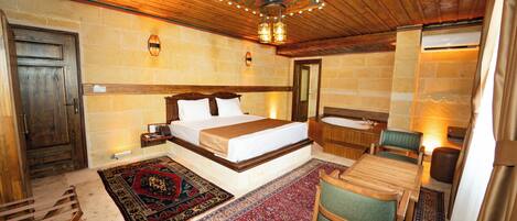 A hotel room with a large bed, a sitting area with a chair and table, a bathtub, and a wooden ceiling.