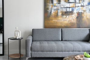A modern living room with a grey sofa, a small round table with a white sculpture, and a large abstract painting on the wall. - Soft Luxury 1BDR in trendy DeWaterkant Nest (Cape Town)