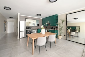 A modern kitchen with a dining area, featuring a wooden table, two chairs, a vase with flowers, and a large mirror. - Soft Luxury 1BDR in trendy DeWaterkant Nest (Cape Town)