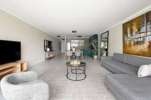 Un salón moderno con un sofá gris, una mesa de centro redonda y un televisor sobre un mueble de madera.