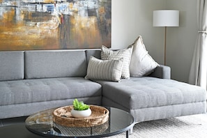 Ein graues Ecksofa mit einem gewobenen Couchtisch und einer Topfpflanze.