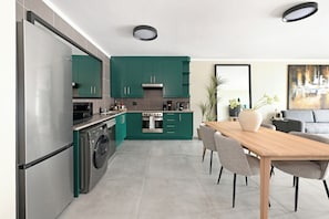 Eine moderne Küche mit Edelstahlgeräten, türkis-farbenen Schränken und einem Essbereich mit einem Holztisch und Stühlen.