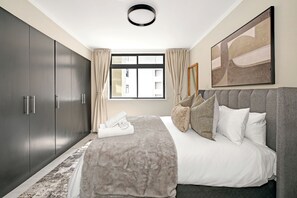 Ein modernes Schlafzimmer mit einem großen Bett, einem grauen Kleiderschrank und einem Fenster mit Vorhängen.