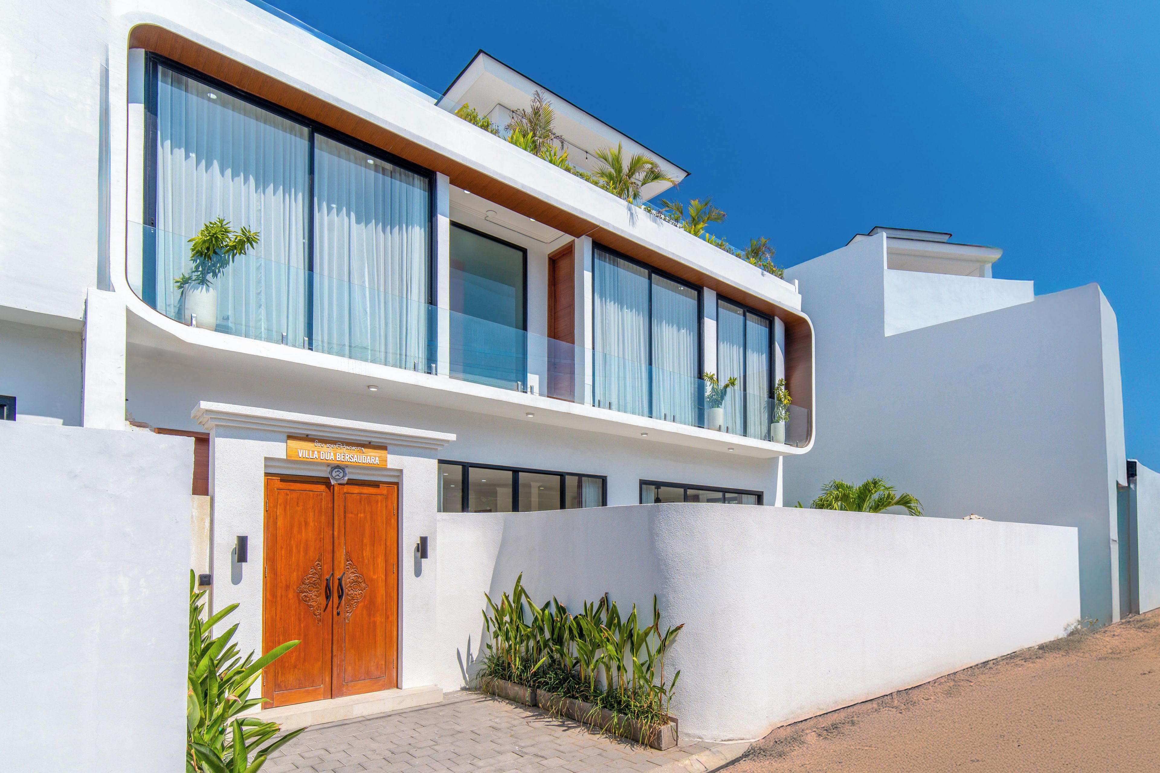 Une villa moderne à deux étages, dotée de grandes fenêtres et d’une porte en bois.