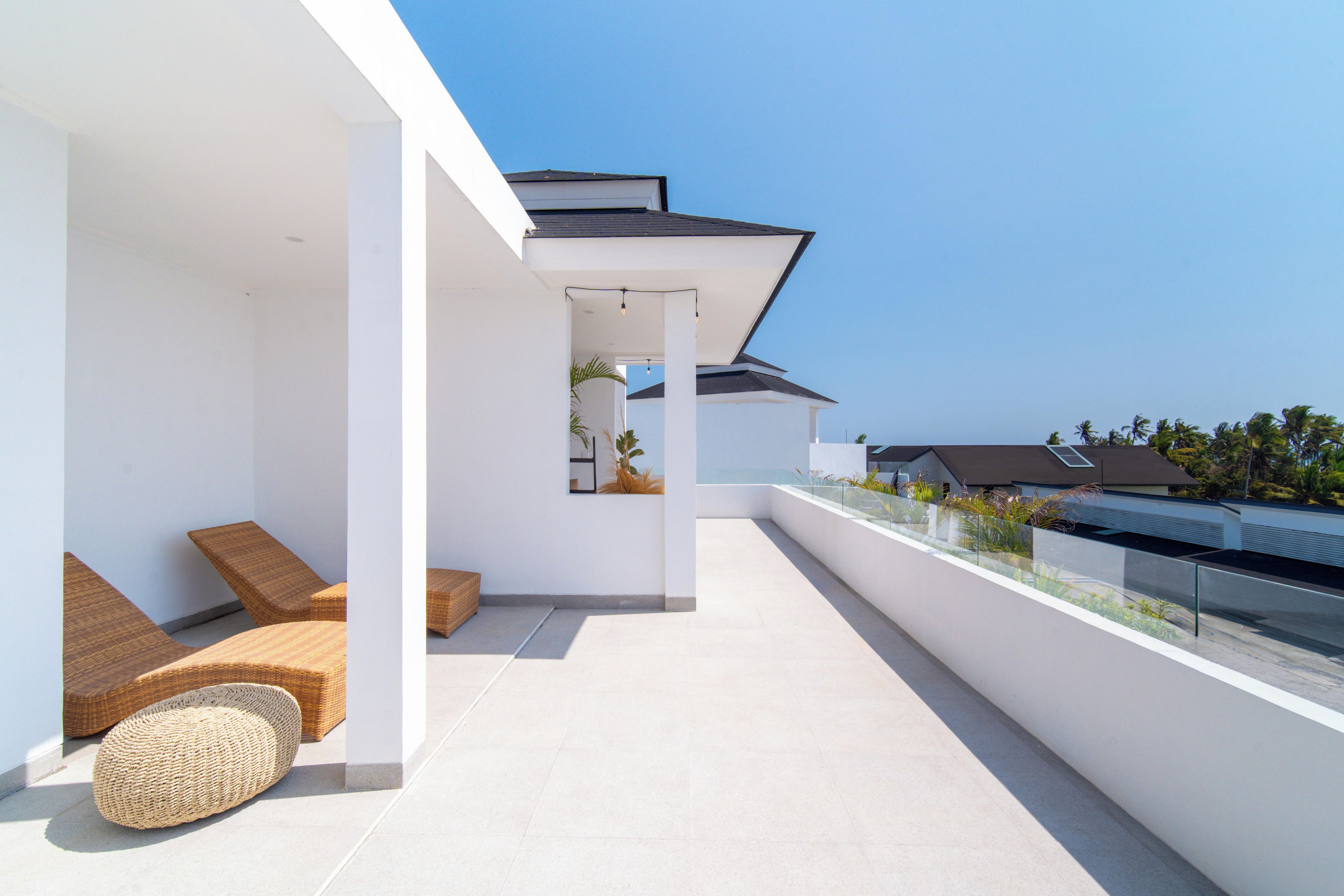 Un espace extérieur moderne, aménagé avec des meubles en osier et doté d’une balustrade en verre, offrant une vue sur un quartier résidentiel.
