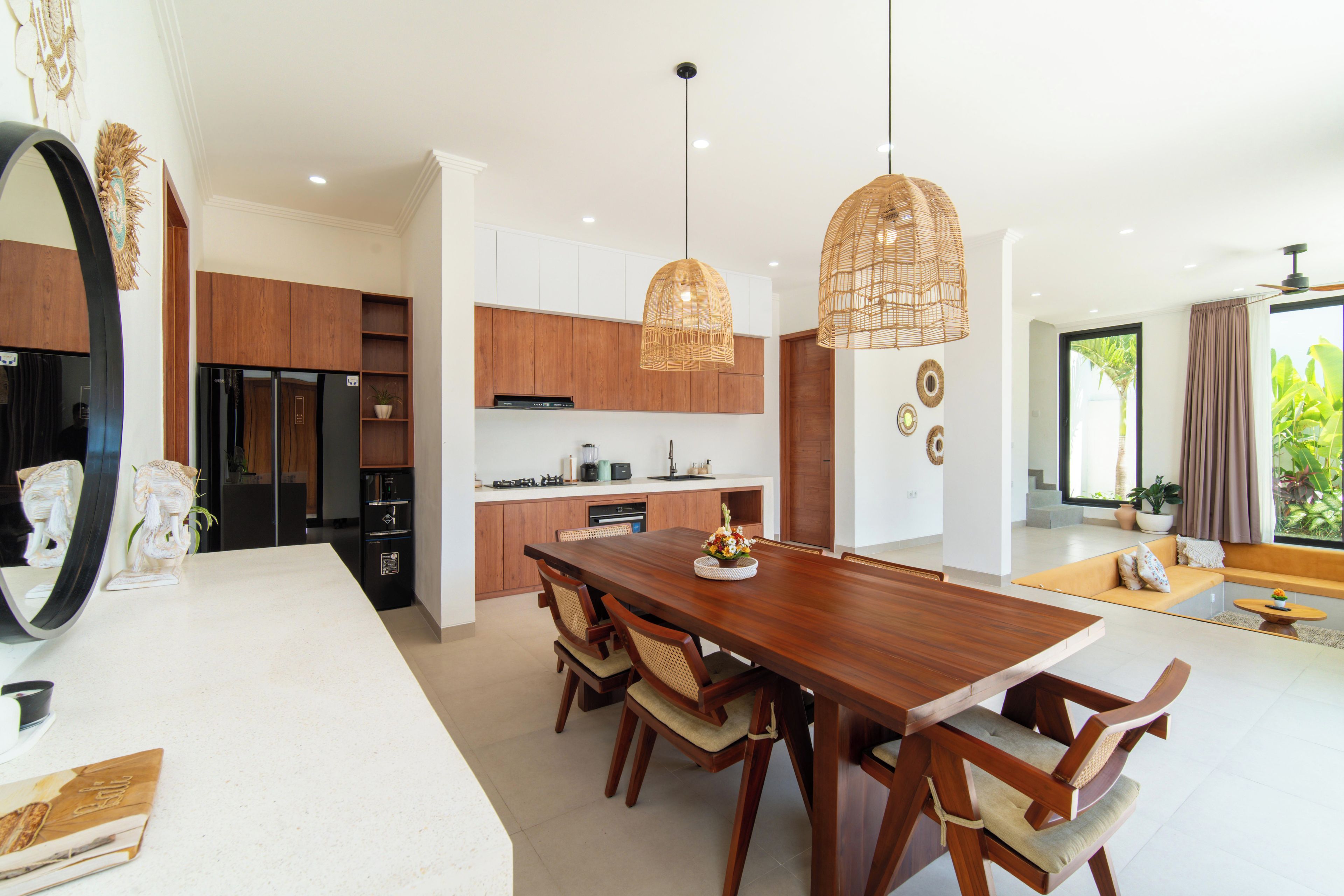 A modern kitchen with wooden cabinets, a dining area with a large wooden table, and pendant lighting.