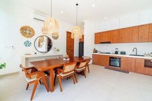 A modern kitchen with wooden cabinets, a built-in oven, and a dining area with a wooden table and chairs. - 2-Min Walk to Seseh Beach • 2BR Private Pool Villa with Rooftop Sea View (Badung)