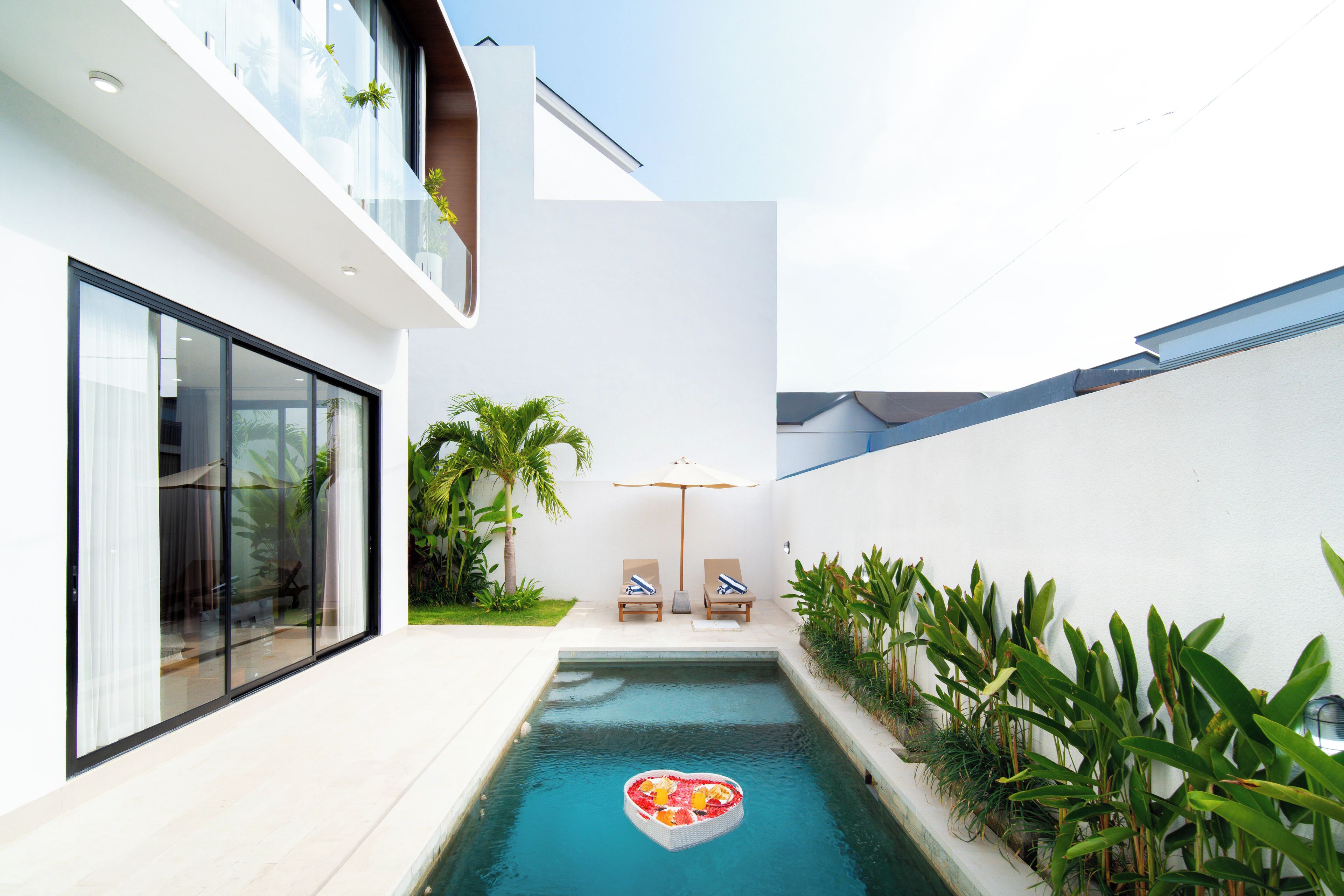 A modern pool with a heart-shaped float, surrounded by lush greenery and a minimalist architectural design.