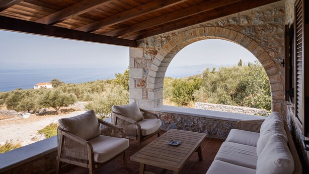 A covered outdoor seating area with stone walls and a view of the sea. - Pirgos Petropoulea (Agios Nikon)