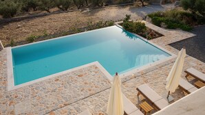 A rectangular swimming pool with a stone border, surrounded by lounge chairs and umbrellas. - Pirgos Petropoulea (Agios Nikon)
