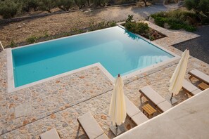 A rectangular swimming pool with a stone border, surrounded by lounge chairs and umbrellas.