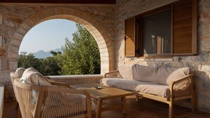 Una habitación con paredes de piedra, un ventanal arqueado grande, un sofá, dos sillones de mimbre y una mesa de madera.