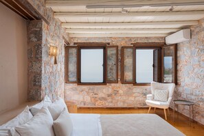 Une chambre avec un mur en pierre, un lit, une chaise et une fenêtre avec des volets.