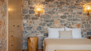 A bedroom with a stone wall, wooden wardrobe, and a bed with white bedding. - Pirgos Petropoulea (Agios Nikon)