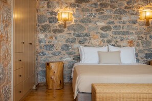 A bedroom with a stone wall, wooden wardrobe, and a bed with white bedding.