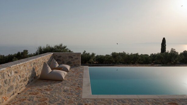 Piscina de piedra con vista al mar y un muro de piedra con cojines.