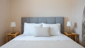 Una cama bien hecha con sábanas blancas y dos lámparas de noche sobre mesitas de madera.