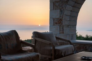 A terrace with wicker furniture and a stone wall, overlooking a body of water and distant mountains. - Pirgos Petropoulea (Agios Nikon)