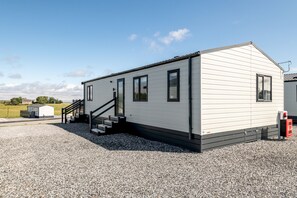 A single-story mobile home with a front staircase, a small porch, and a gravel driveway. - Lodge No 173 | Hot Tub | Stewart's Resort Cameron (Cameron)