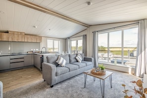Ein stilvoller Wohnraum mit grauem Sofa, einem Essbereich und großen Fenstern mit Blick ins Freie.