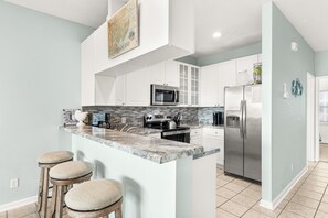 A modern kitchen with a central island, stainless steel appliances, and a backsplash. - Unobstructed Ocean Views Direct Beach/Pool Access + Parking by Tybee Cottages (Tybee Island)