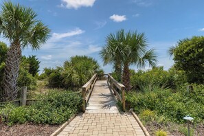 A wooden boardwalk leading through a landscaped area with various plants and trees. - Unobstructed Ocean Views Direct Beach/Pool Access + Parking by Tybee Cottages (Tybee Island)