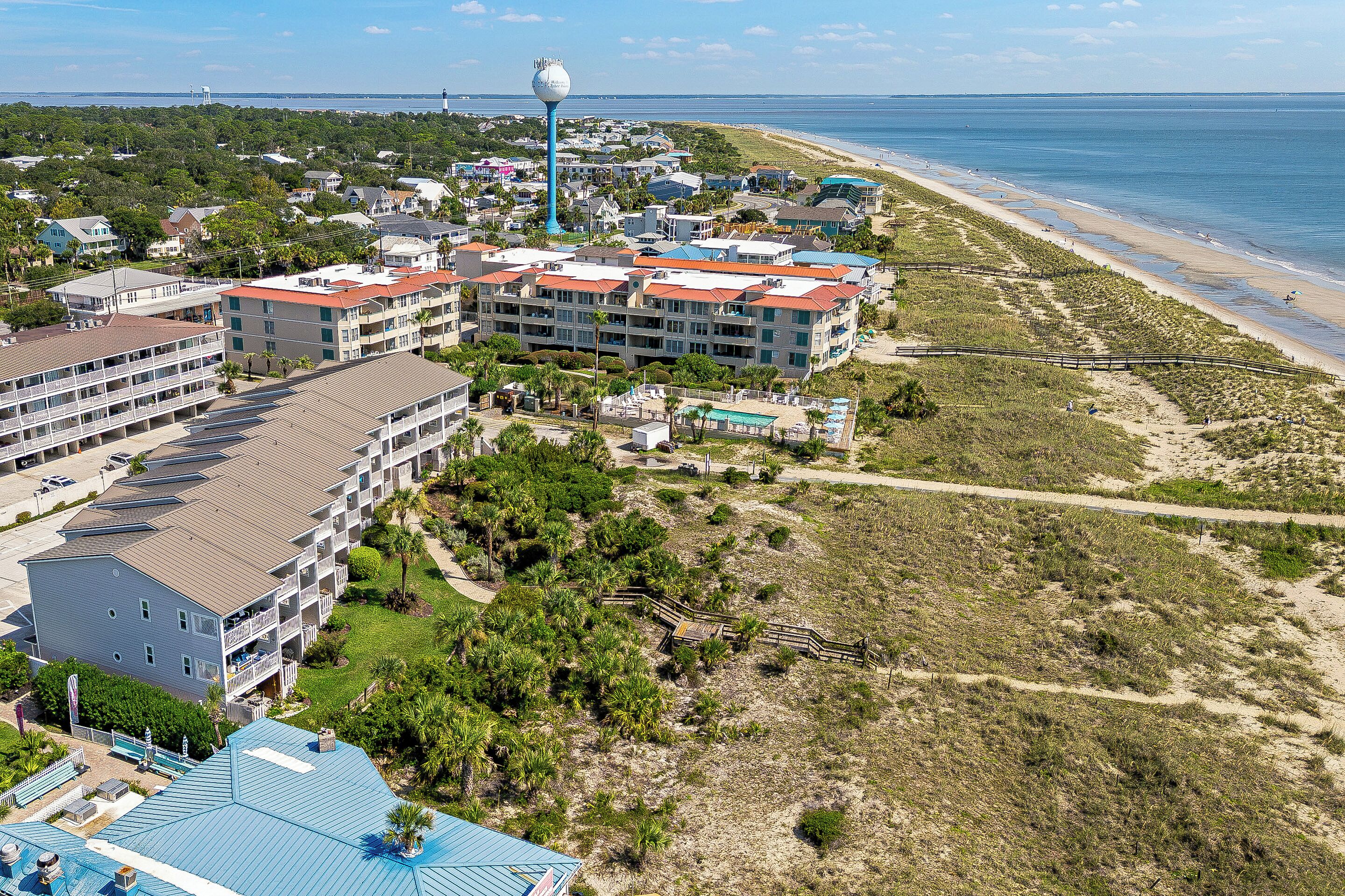A coastal hotel with multiple buildings, a beach, and a lighthouse in the background.