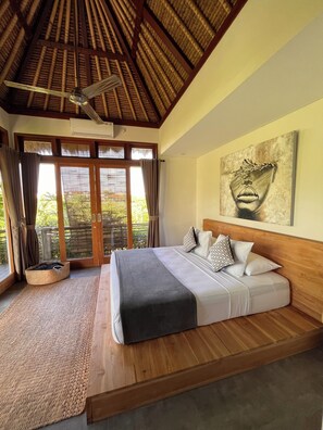Ein Schlafzimmer mit Bett, Deckenventilator, großem Fenster mit Vorhängen und einem Bild an der Wand.