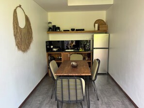 Eine kleine Küche mit Holztisch und Stühlen, einem Kühlschrank und diversen Küchengeräten.