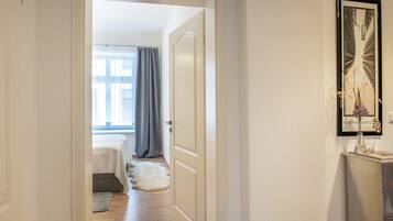 A hallway leading to a bedroom with a bed, a window with curtains, and a framed picture on the wall.