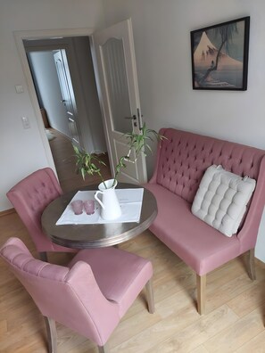 A room with a pink sofa, a matching armchair, a small round table with a white pitcher and pink items, and a painting on the wall. - Apartment 'Quartier 76- City Loft' with Balcony and Wi-Fi (Schwerin)