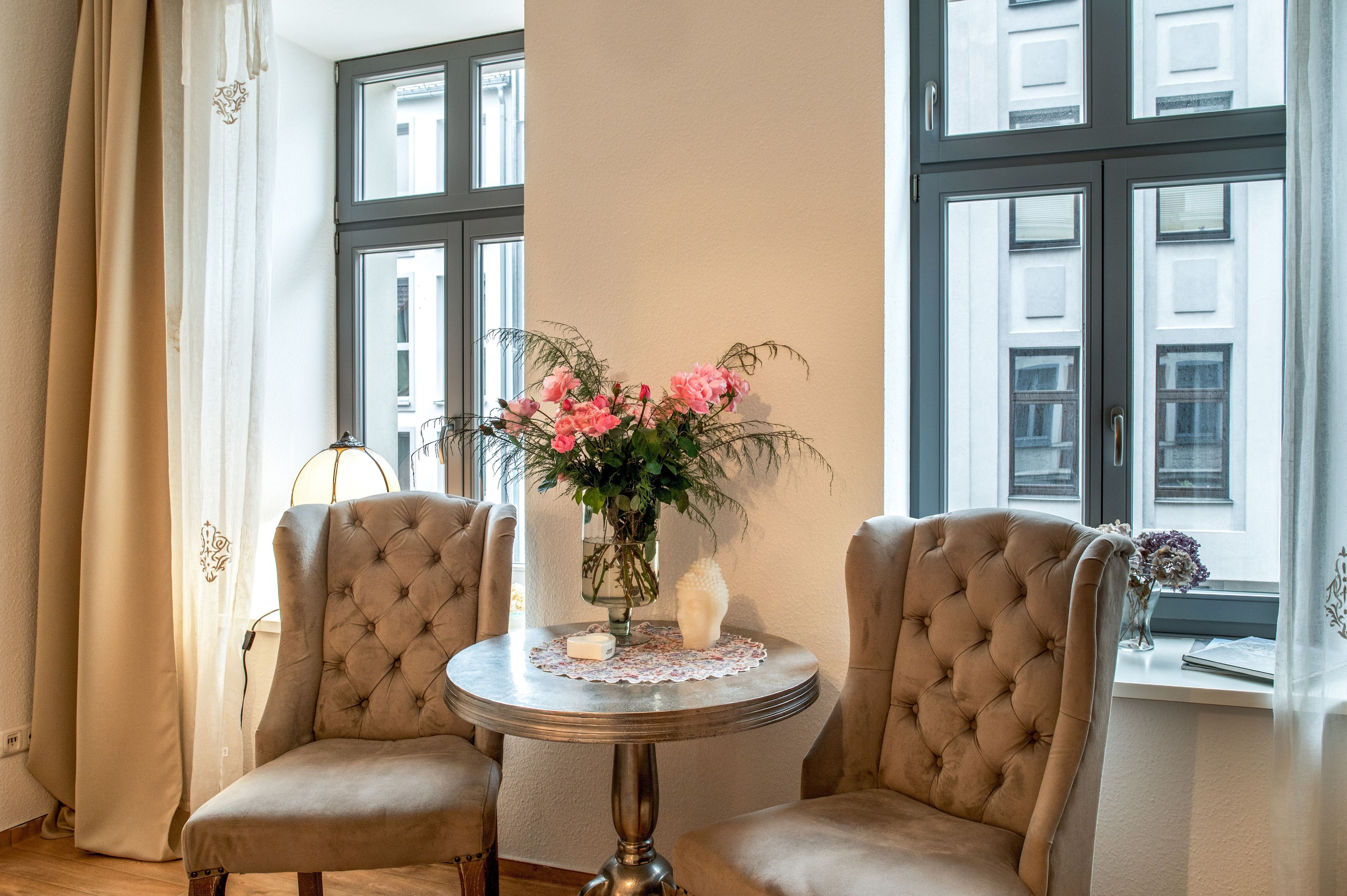 Una habitación con dos sillones tapizados, una mesa redonda con mantel de encaje y un jarrón con flores.