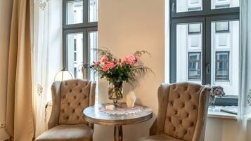 Una habitación con dos sillones tapizados, una mesa redonda con mantel de encaje y un jarrón con flores.