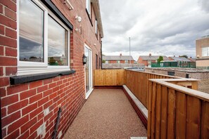 Un estrecho pasillo exterior con pared de ladrillo rojo, valla de madera y camino de grava.