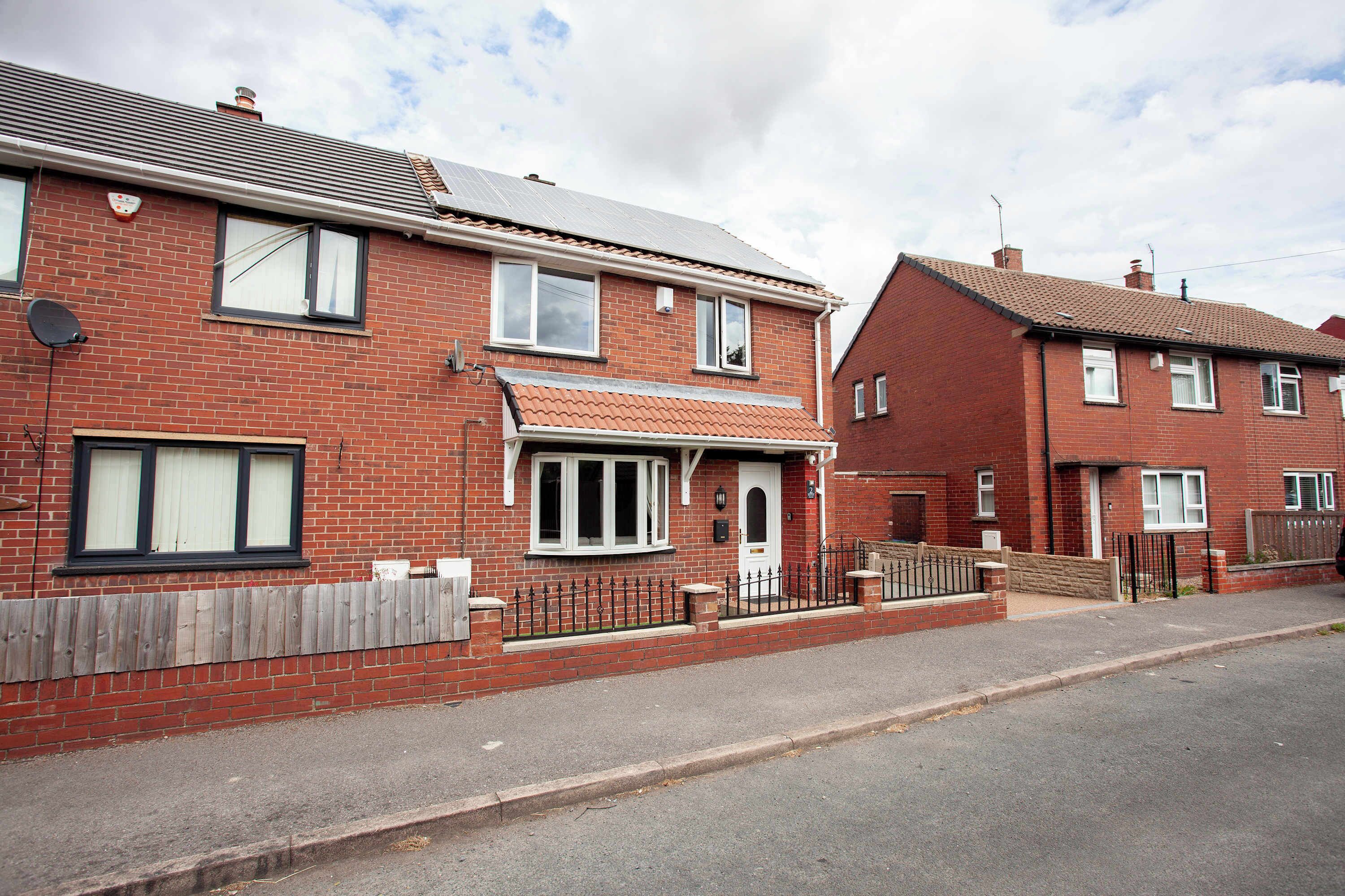 A row of red brick houses with a front garden and a metal fence.