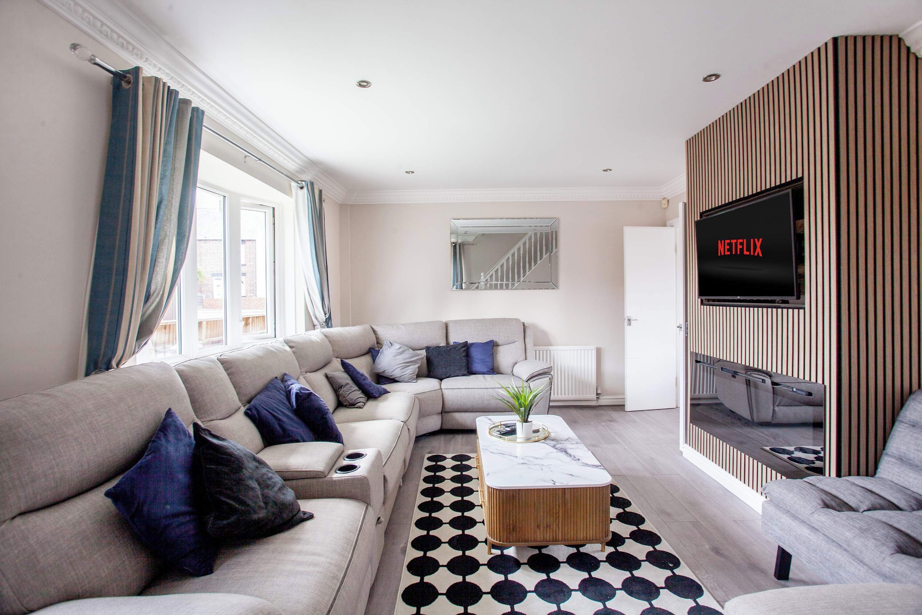 A modern living room with a sectional sofa, a coffee table, a TV, and a patterned rug.