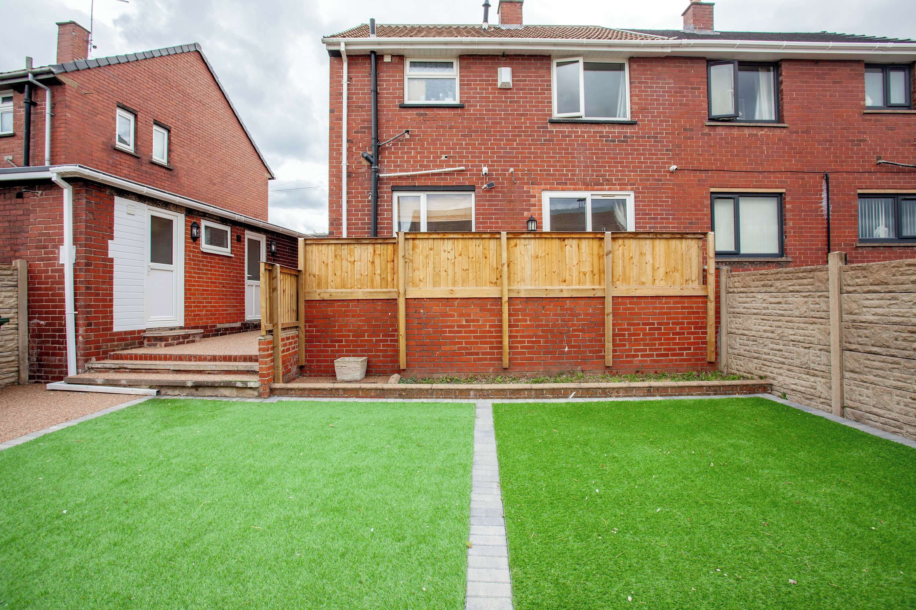 A residential property with a brick house, a wooden fence, and a well-maintained lawn.