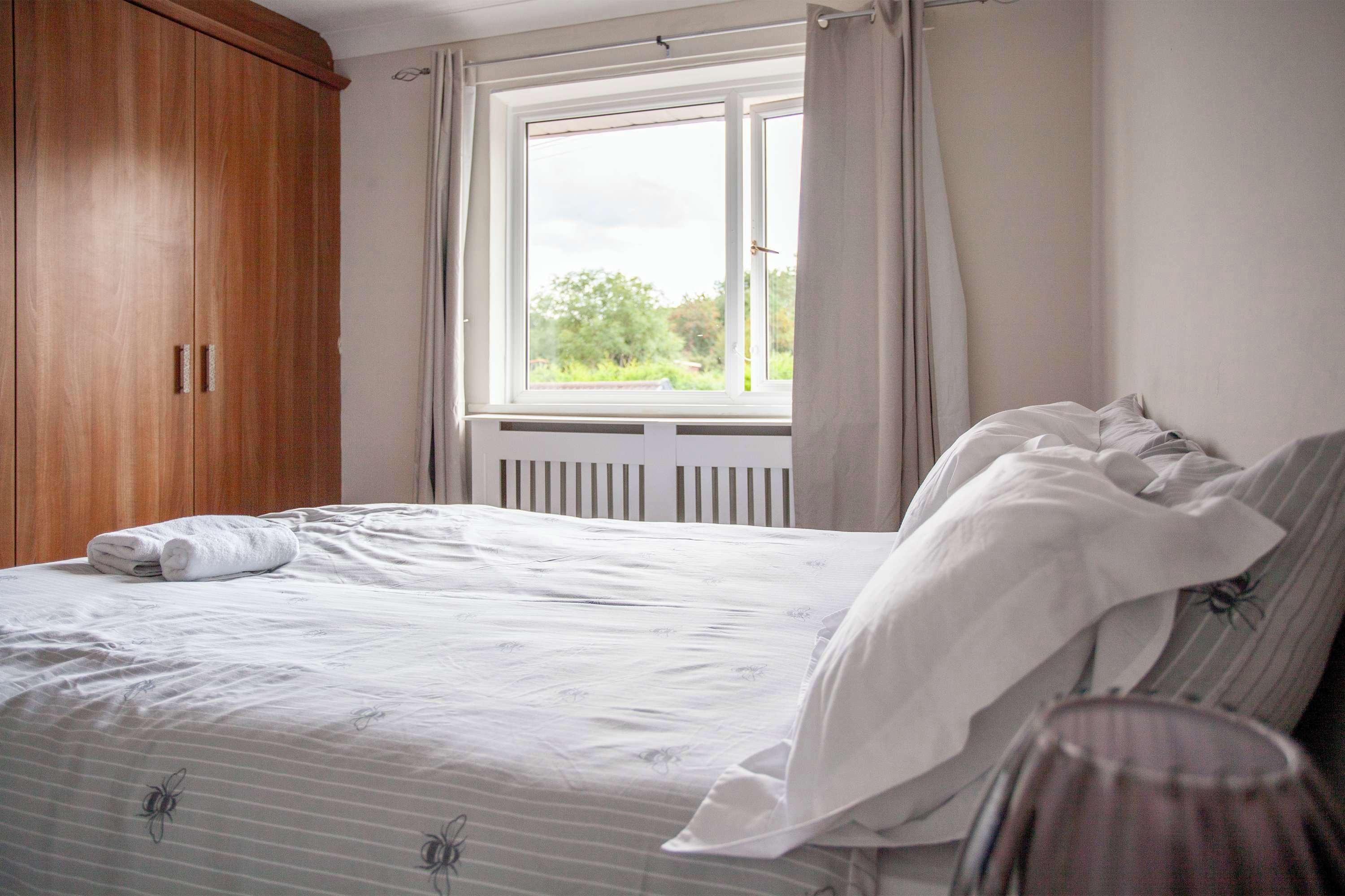 A bedroom with a bed, a window, and a wooden wardrobe.