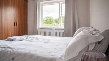A bedroom with a bed, a window, and a wooden wardrobe.