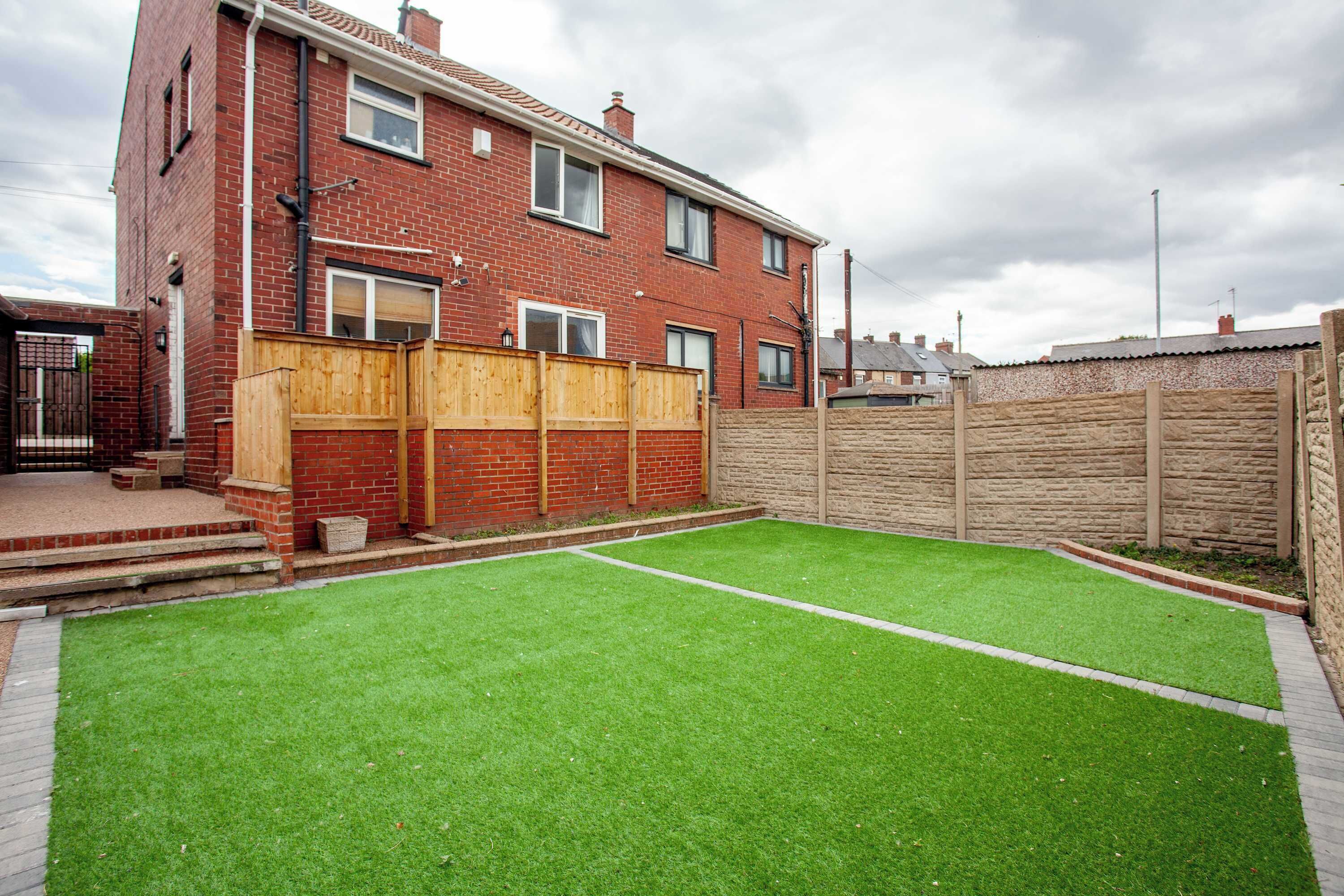 A residential property with a fenced backyard, a brick house, and a well-maintained lawn.