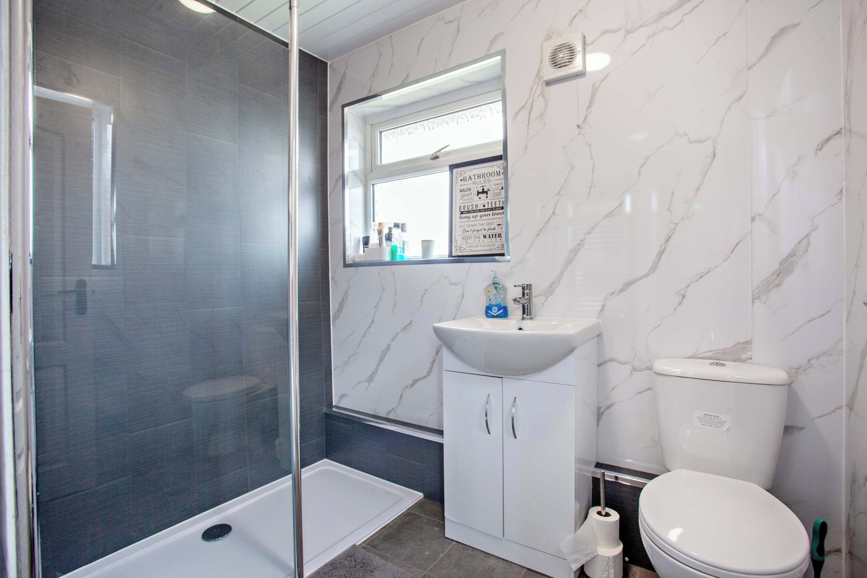 A bathroom with a glass shower enclosure, a white sink with a mirror above it, and a toilet.