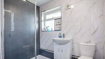 A bathroom with a glass shower enclosure, a white sink with a mirror above it, and a toilet.