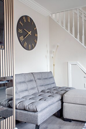 Una sala moderna con un sofá seccional gris, un reloj de pared negro y una escalera.
