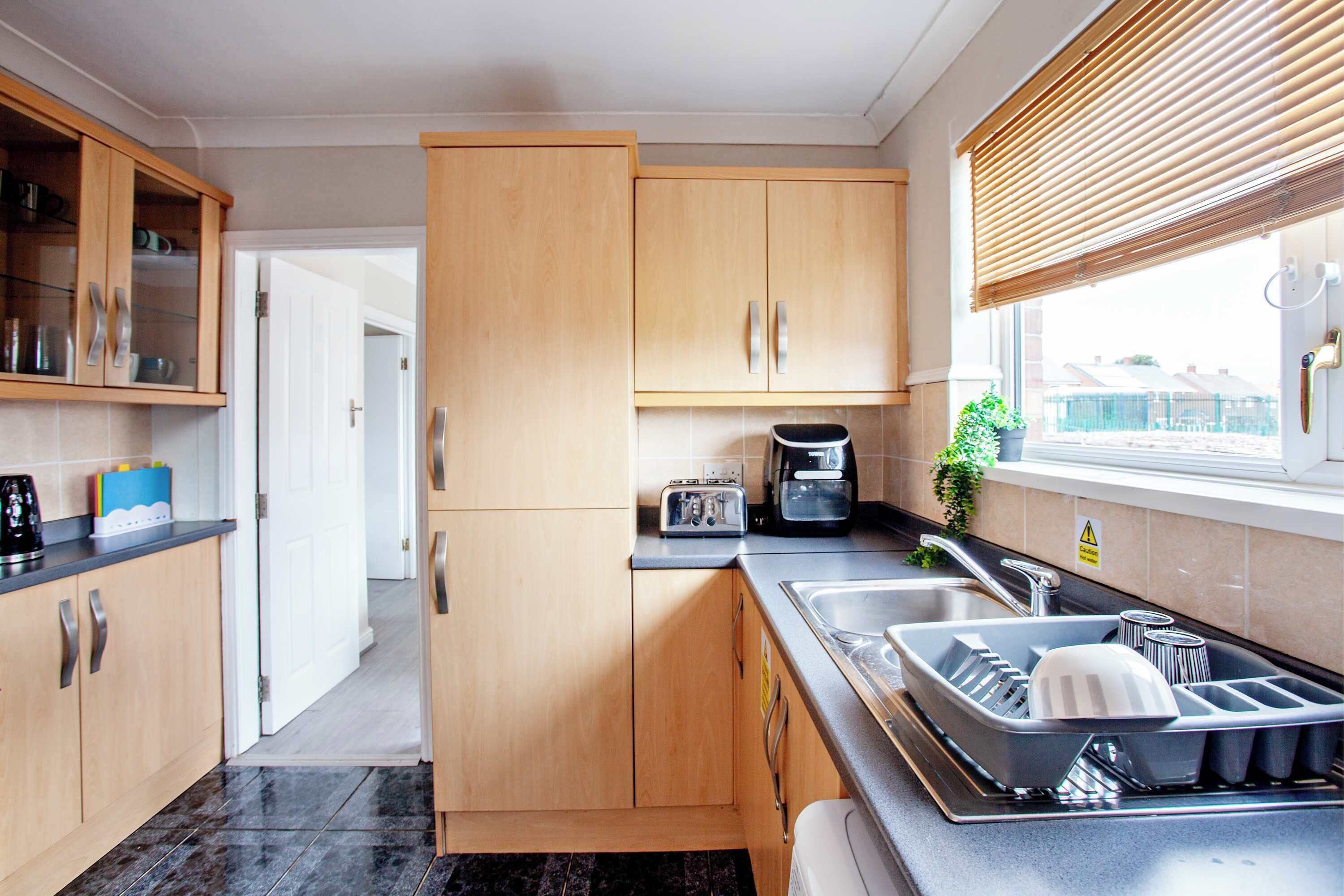 A modern kitchen with wooden cabinets, a built-in oven, a toaster, and a sink with a dish rack.