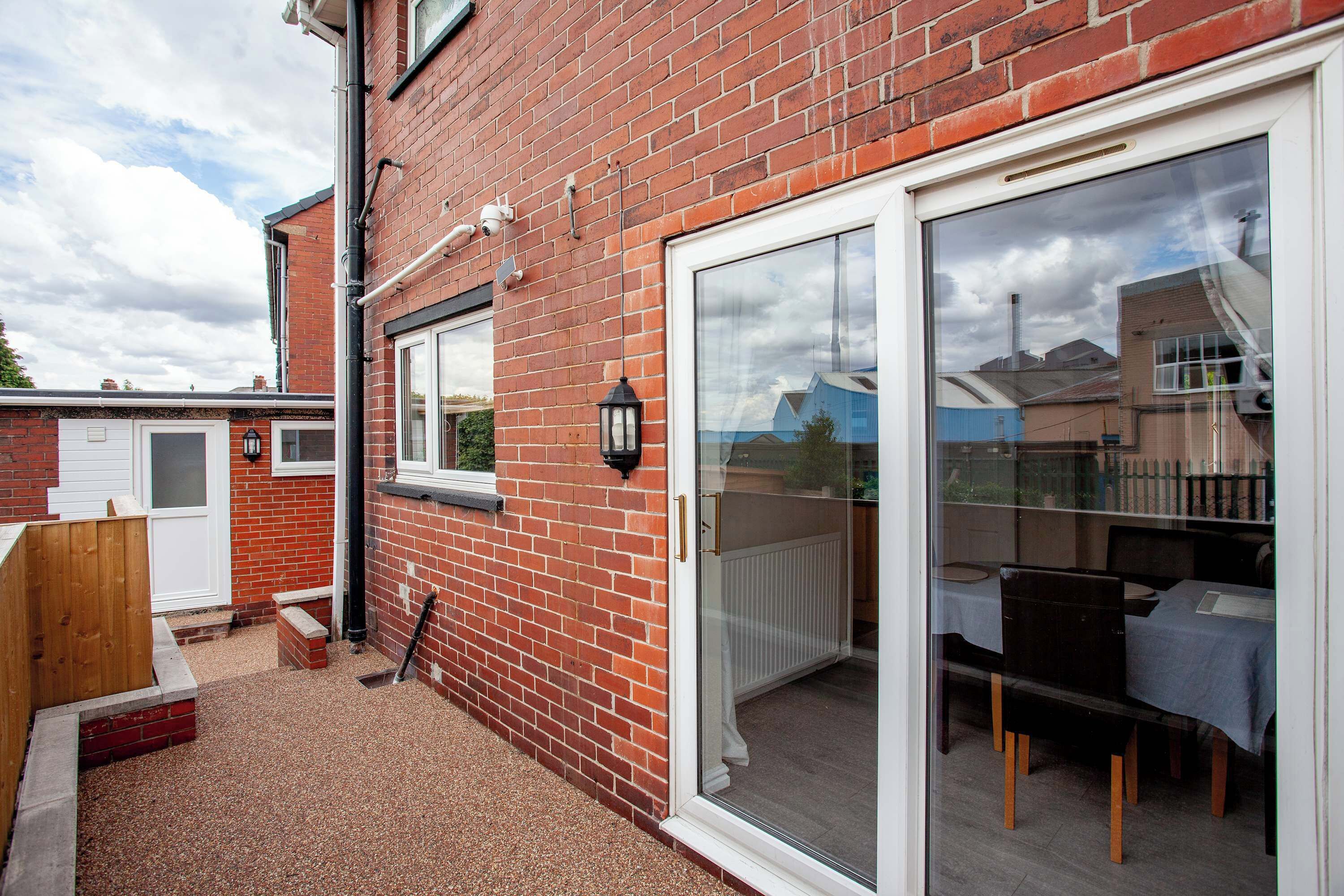 A brick house with a sliding glass door leading to a patio with a table and chairs.