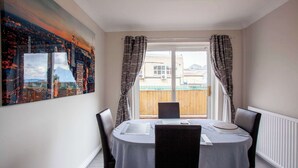 Ein Essbereich mit einem Tisch für vier Personen, einem Stadtbildgemälde an der Wand und Blick auf einen Holzzaun durch das Fenster.