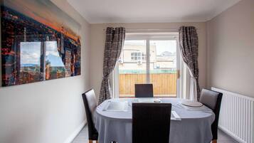 A dining area with a table set for four, a cityscape painting on the wall, and a view of a wooden fence through the window.
