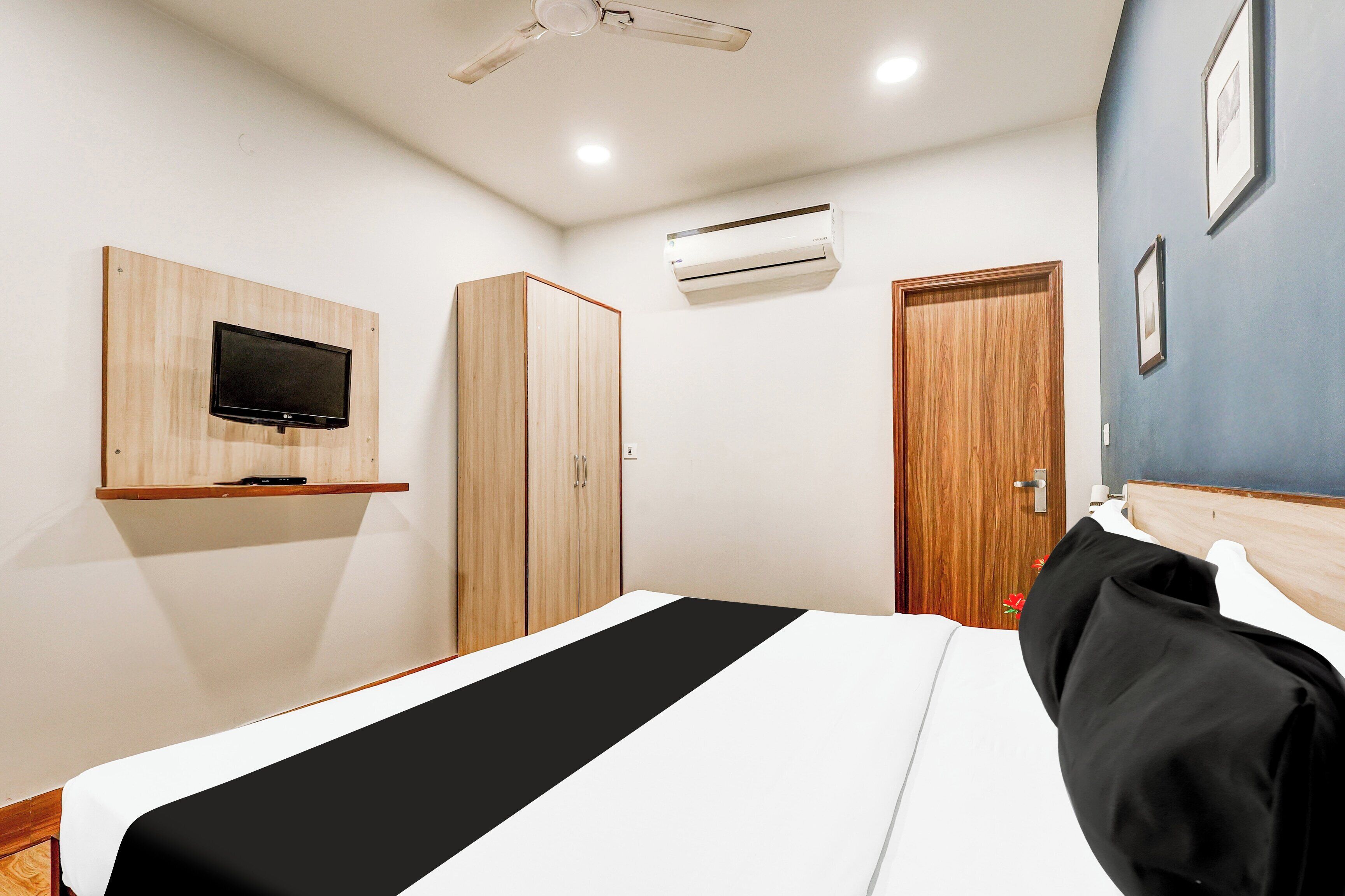 Habitación de hotel con cama, televisor montado en la pared, armario, aire acondicionado y una puerta.