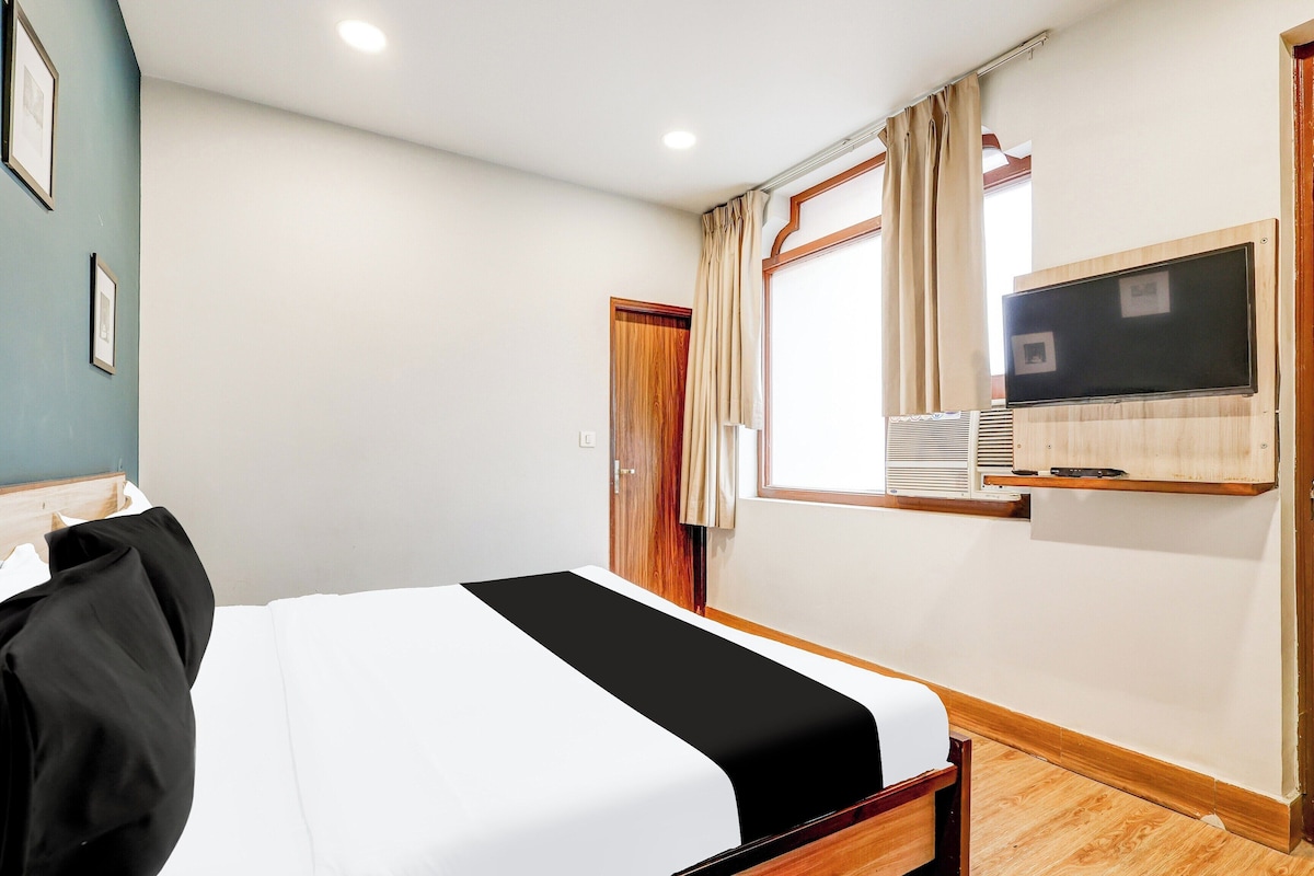 Ein Hotelzimmer mit einem Bett, einem an der Wand montierten Fernseher und einem mit Vorhängen versehenen Fenster.