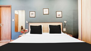 A hotel room with a bed, two black pillows, a wooden headboard, and three framed pictures on the wall. - Collection O GNRC Hospital Dispur (Guwahati)